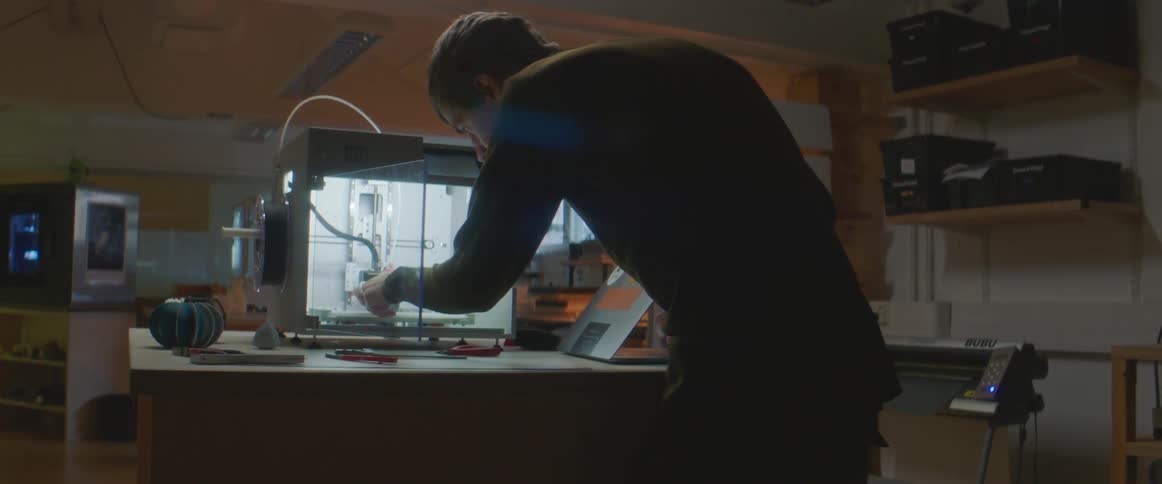 Young man working with a 3d printer with a laptop inside a workshop