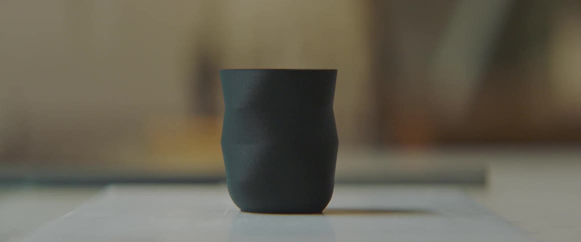 A dark colored cup made of pottery sits on a table