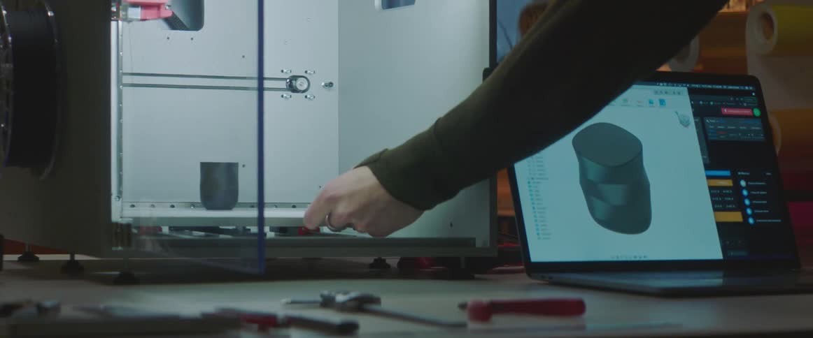Man pull object out of 3d printer sitting next to laptop showing digital image of object