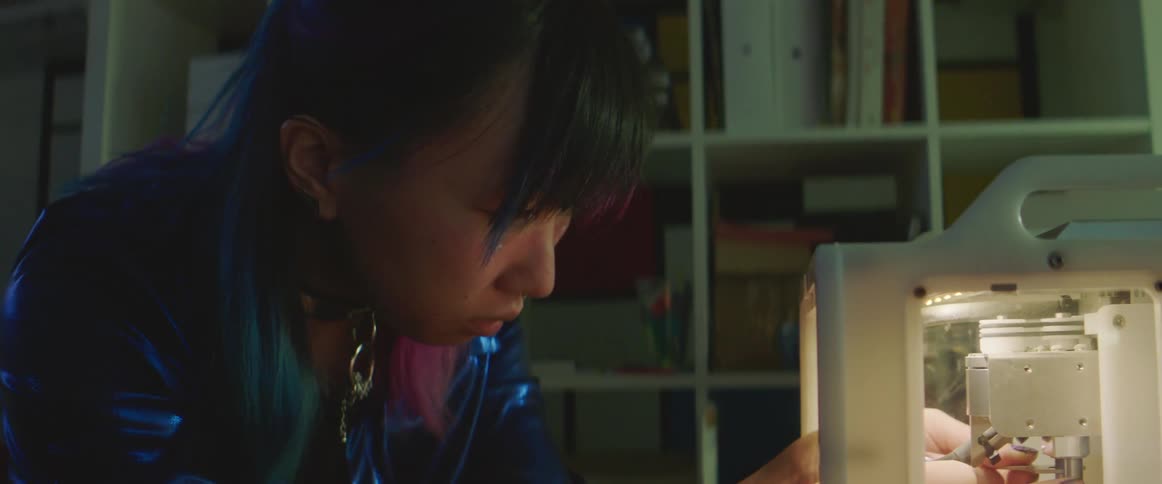 Young woman with blue and magenta dyed hair works on 3d printer