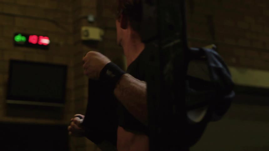 A man is lifting weights in a gym then removes his hat