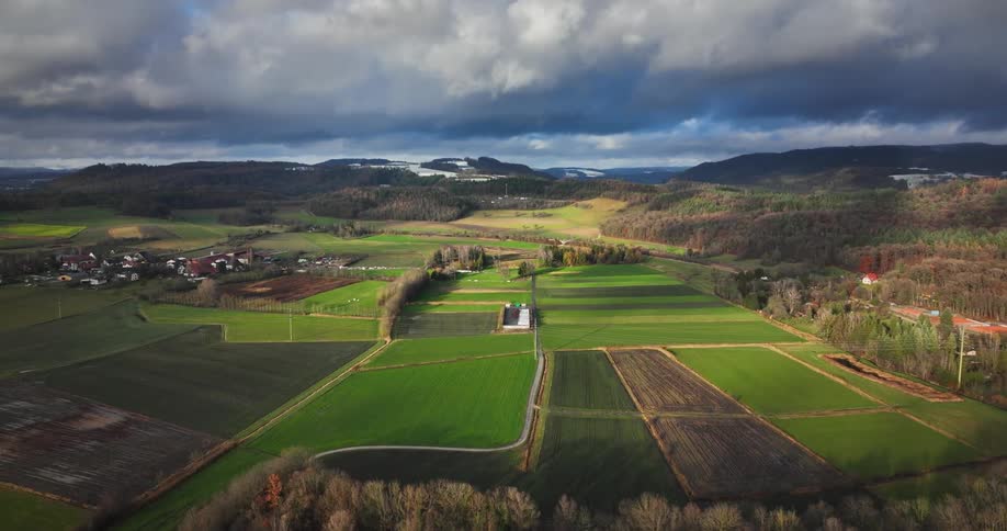 Aerial view of farmlands and small village under clouds