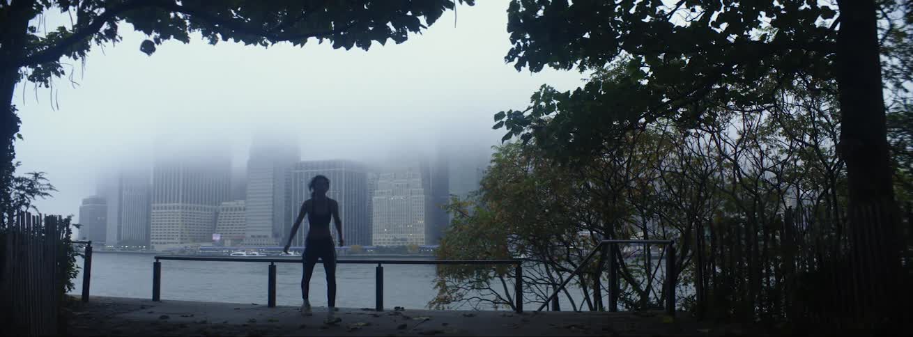 Woman with sports bra and leggings is silhouetted against the high rise building across the river in fog