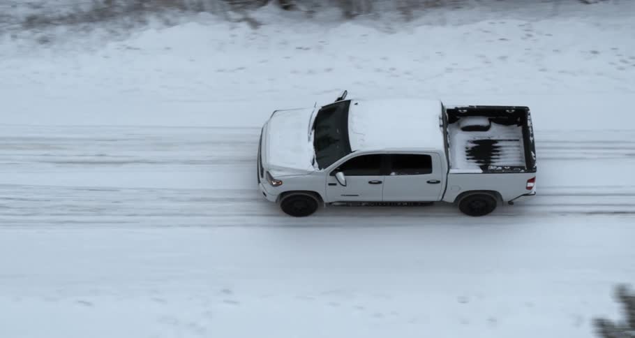 Truck drives along snow covered road passing woods