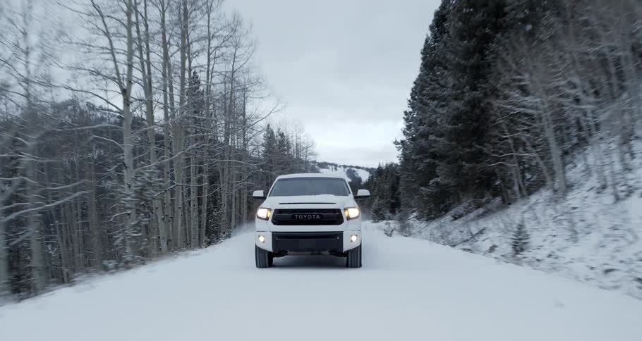 A white pickup truck speeds along a snow covered narrow road