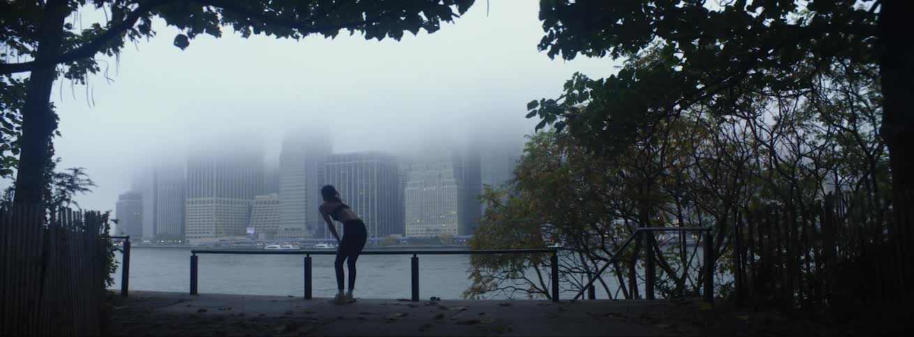 Woman with sports bra and leggings is silhouetted against the high rise building across the river in fog