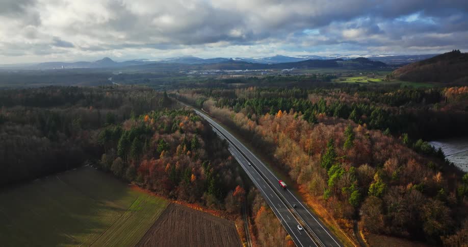 Aerial view of light traffic on a highway surrounded by forests and mountains on the horizon under a cloudy sky