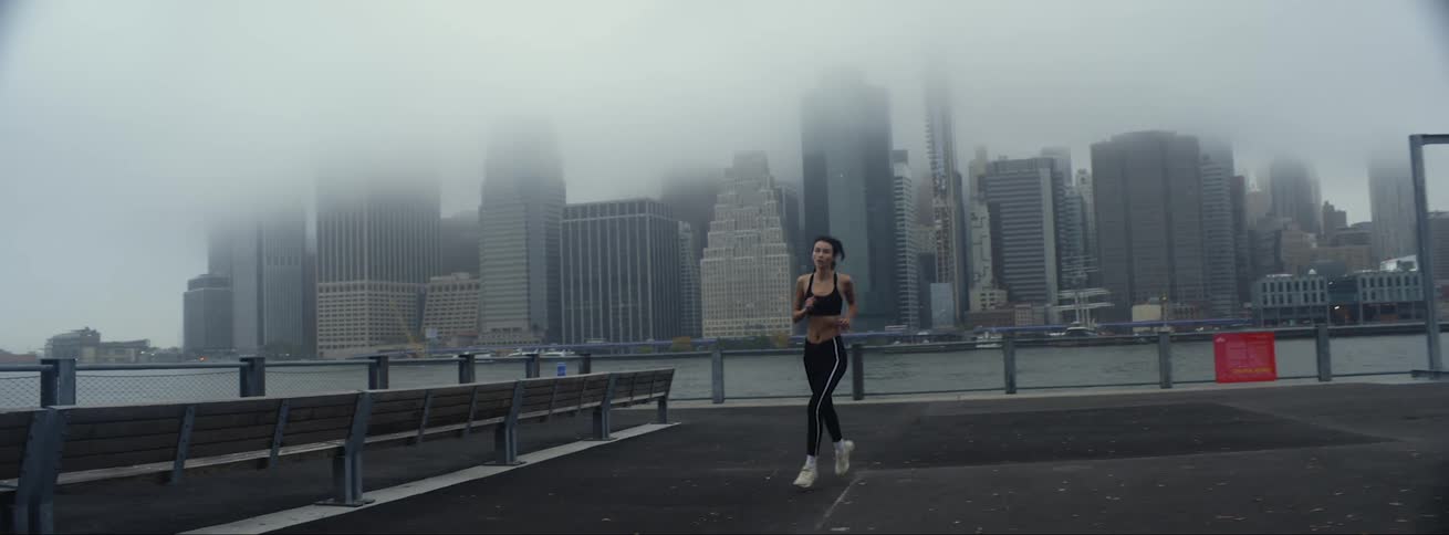 Young woman wearing sports clothes jogging in front of the fog covered skyline of a waterfront city