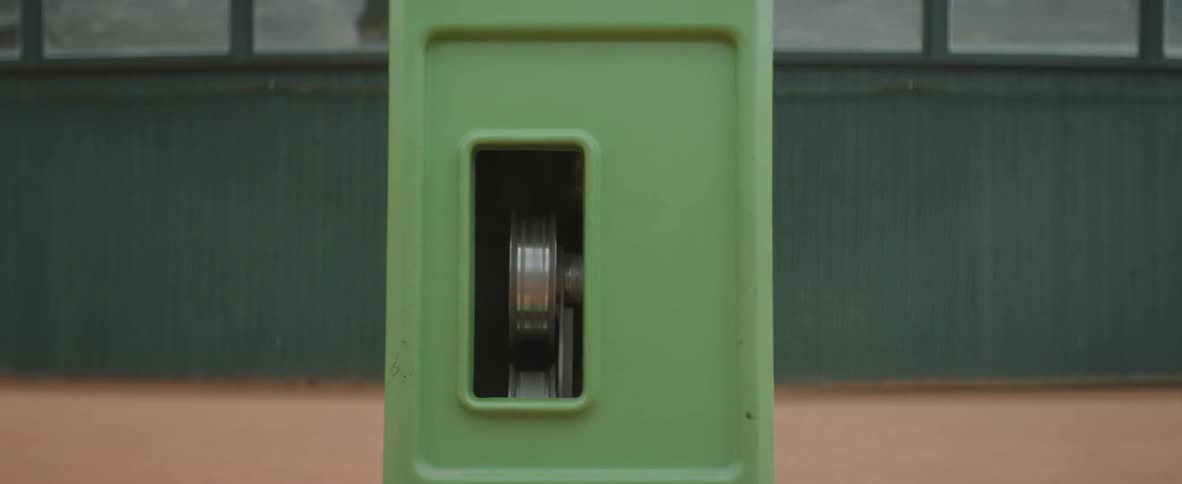 Tennis ball shots directly at the camera from a green tennis machine on the court