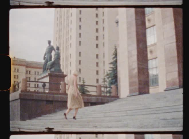 Blonde woman with beige dress and high heels goes up stairs next to monument