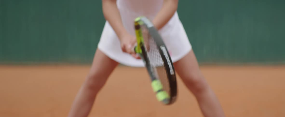 Blonde female tennis player with ponytail and white dress holds racket in tennis court