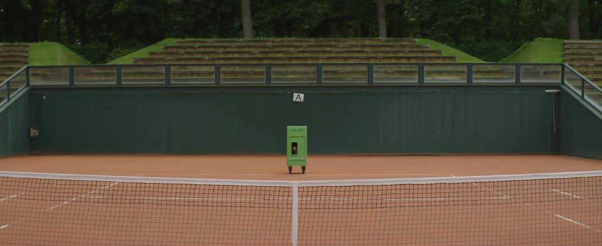 Green tennis ball machine in the middle of a tennis court at daytime