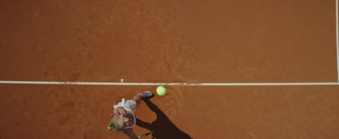Blonde female tennis player with ponytail and white dress plays tennis in tennis court