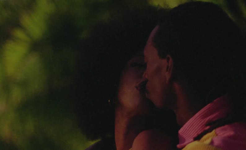 Side view of female dancer with curly hair and yellow dress and man with braids and pink yellow shirt making out in public park