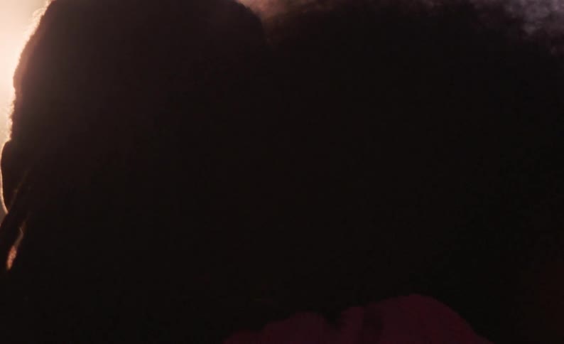 Male dancer with braids and female dancer with curly hair kiss each other at sunset
