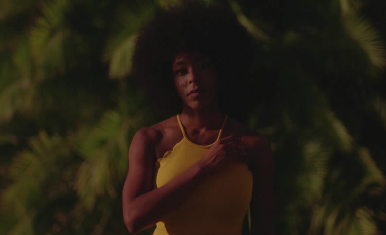 A woman adjusts her shirt strap while posing in front of a large tree