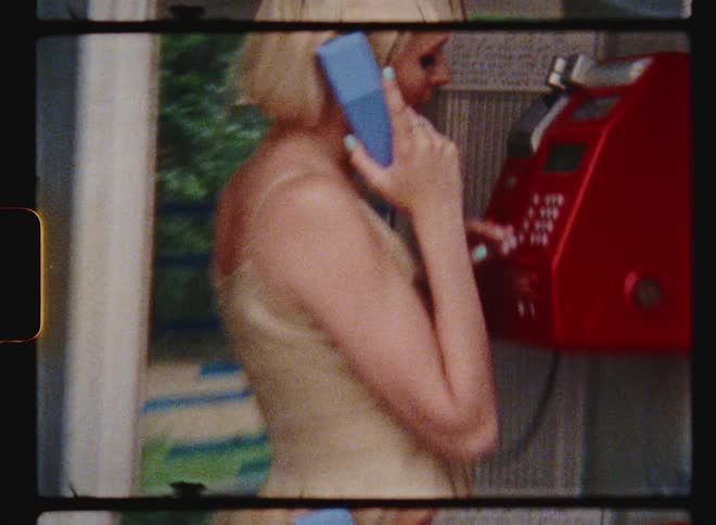 A young woman stands in a phone booth to use a public phone