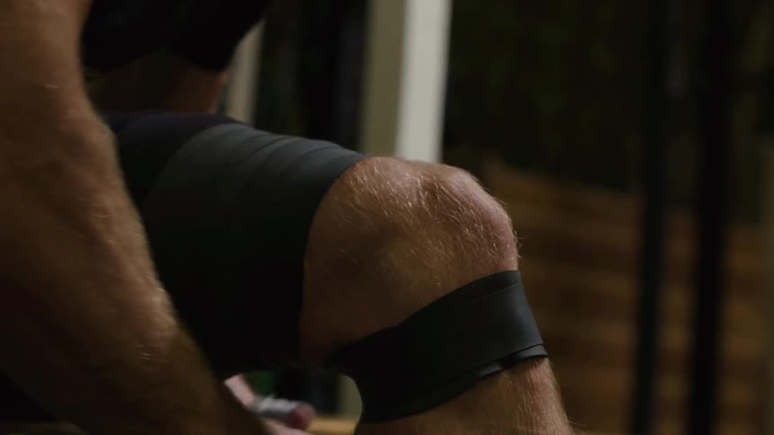 A man is wrapping his leg with black tape