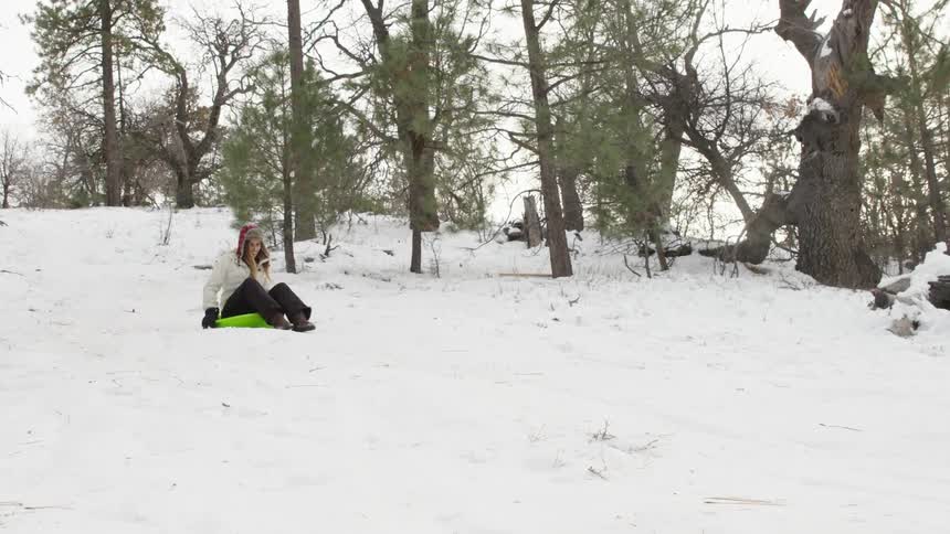 A woman sitting down on a saucer and riding down a snow-packed hillside