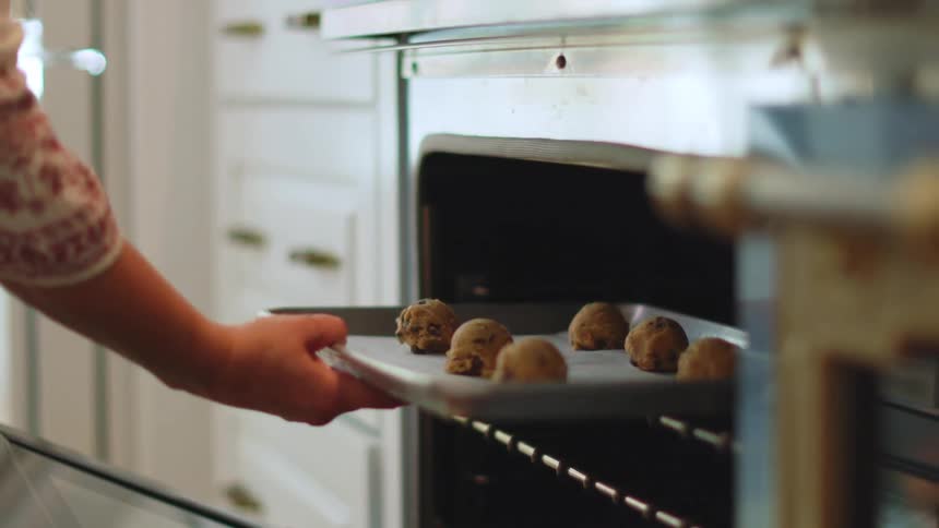 Woman places a tray of raw cookies inside an oven at home