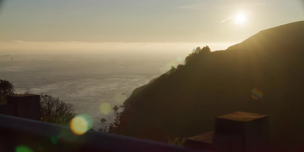 The sun is low in the sky over the ocean shining and glaring on a rocky shore