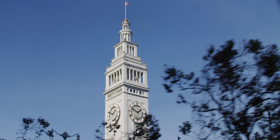 An american flag flies on top of a clock tower on a clear day