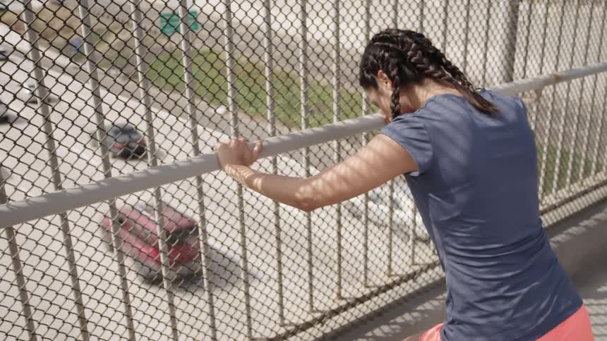 A woman stretches out her calves while standing on an overpass bridge
