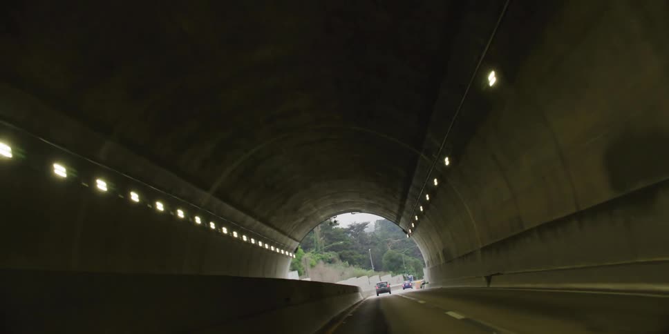 Cars travel through a tunnel and continue on a road lined with trees