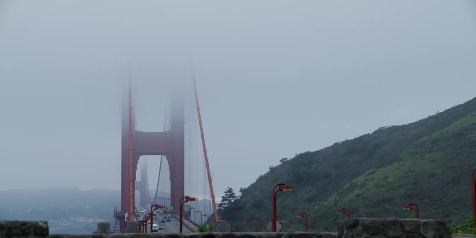 Distant view of vehicle crossing suspension bridge whose towers are in fog on cloudy day