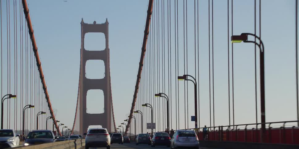 Cars drive across a bridge as people cycle and walk along the pathway on it