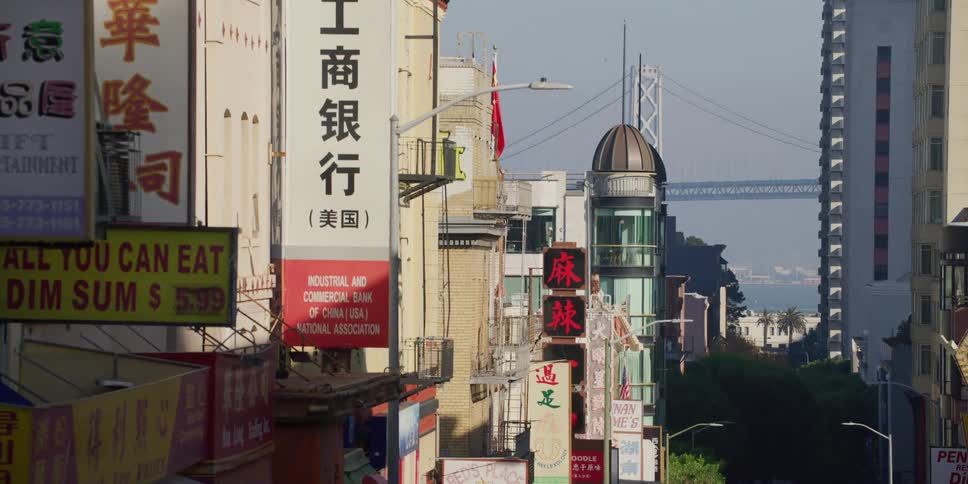 Signs and banners in chinese hang from chinatown buildings with a view of the oakland bay bridge