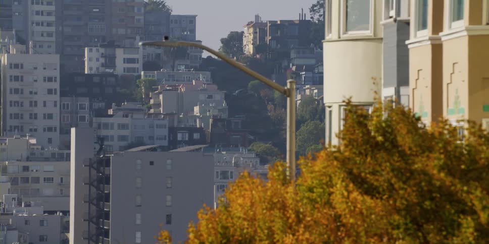 Homes and apartment buildings cover a steep hill in a city on a bright day