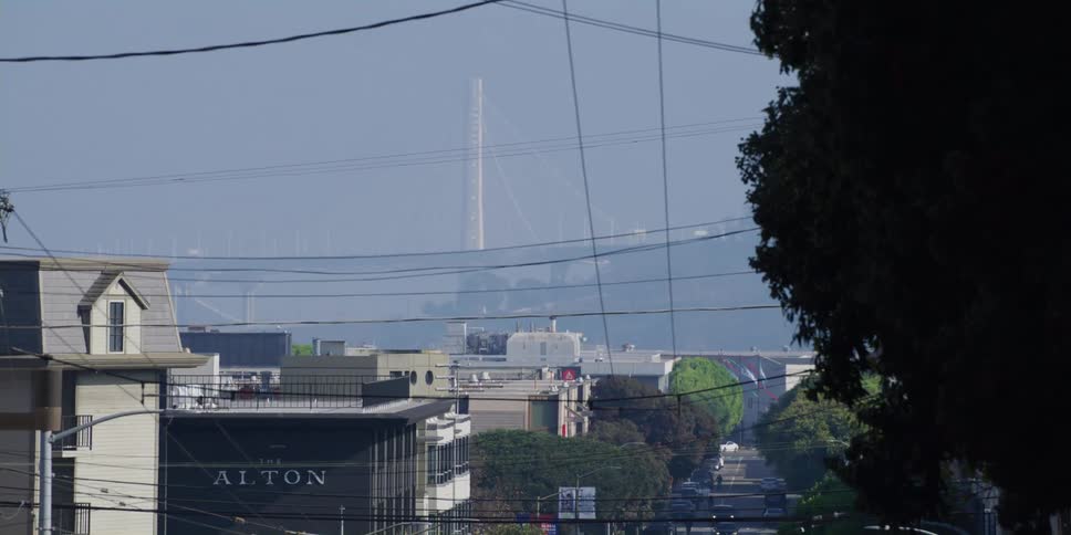 The bridge is visible through the haze at the bottom of a steep san francisco street
