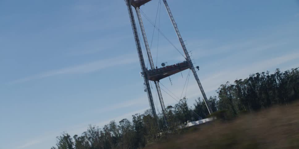 A utility tower stands tall above the trees in a blue sky