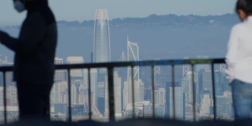 People standing near a fence in front of the city skyline near the mountains