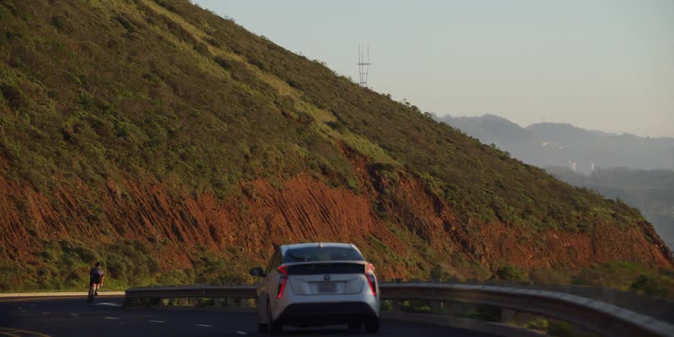 A car passes two bicyclists on a windy mountain road
