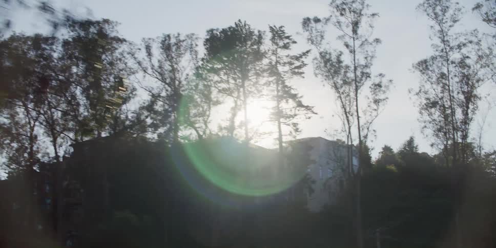 Sunlight halo at sunset over the silhouette of houses in the hills surrounded by trees
