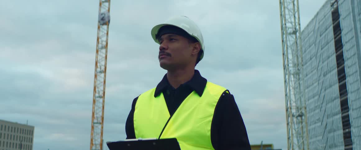 Construction worker wearing a vest and a safety helmet standing at a construction site