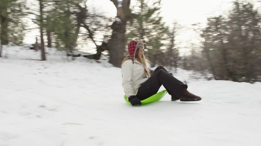 A woman rides a small green sled down a slope