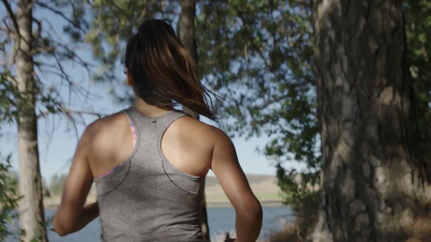 A woman jogging through woods next to a body of water
