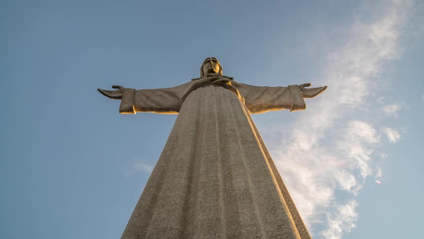 A statue of jesus christ with his arms outstretched against a blue sky and clouds