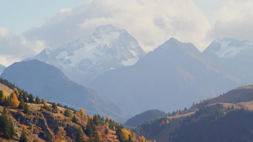 Colorful pine trees growing on the slopes of the mountains close to the snow covered mountain range