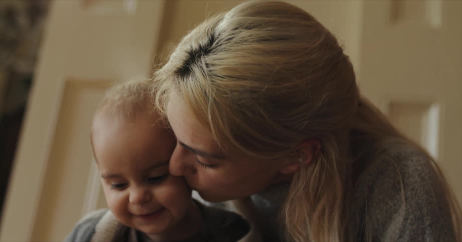 A woman at home picks up her baby son and kisses him on the cheek