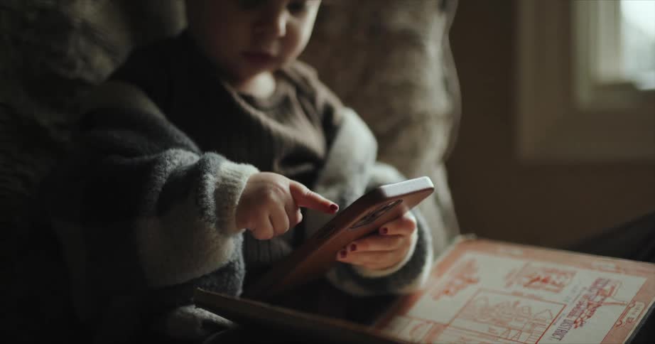 A baby plays with a smart phone while sitting on a chair