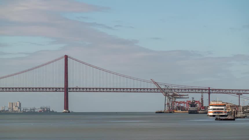 Suspension bridge with suspension cables on vertical suspenders over river with boats traveling