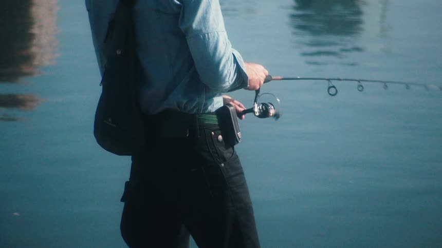 Young man fishing on the calm surface of a lake at daytime