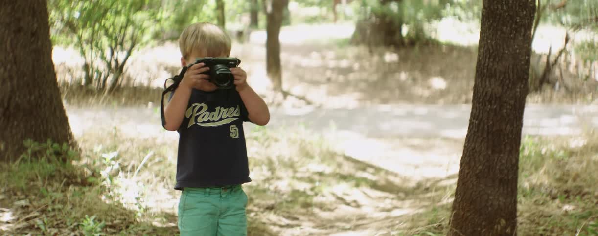 A little boy turning around and pretending to snap a picture with a large camera