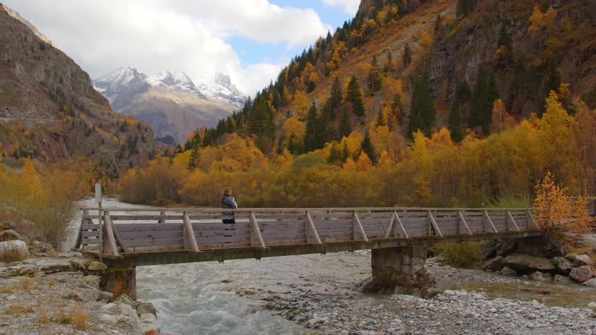 A woman holds her baby while walking on a pedestrian bridge across a river