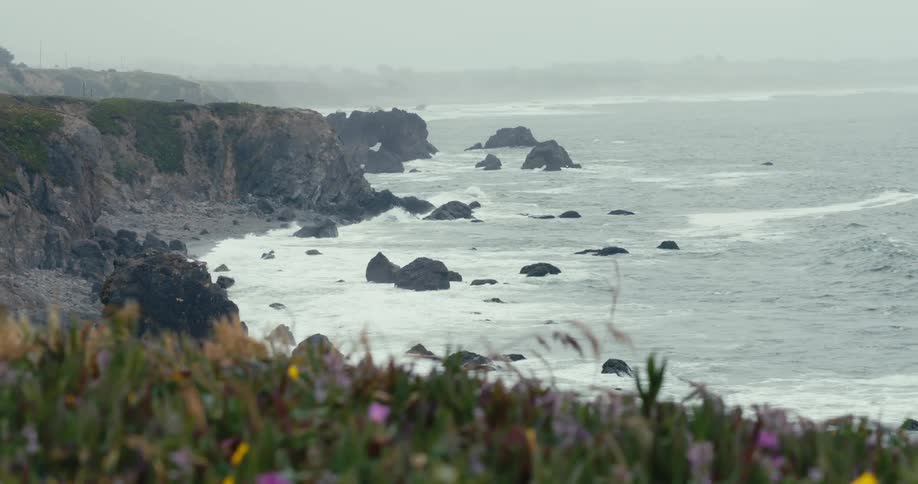 Waves crashing on rocky shoreline on foggy morning