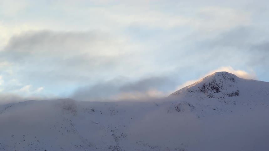Clouds pass over the snow covered mountain peak at morning